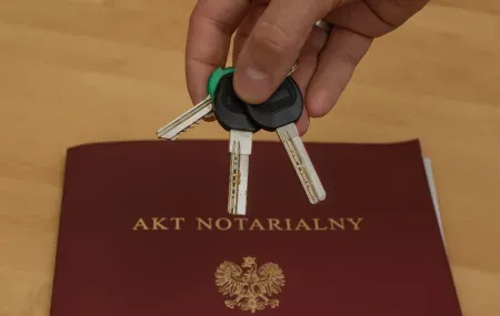 Klucze w dłoni na tle aktu notarialnego.