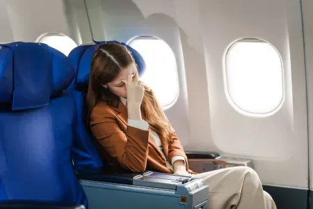 Kobieta w samolocie. Zakrywa twarz.