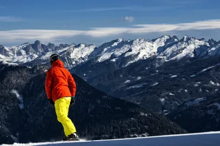 Sylwetka odwróconej osoby, która zjeżdża na snowboardzie. W tle góry.